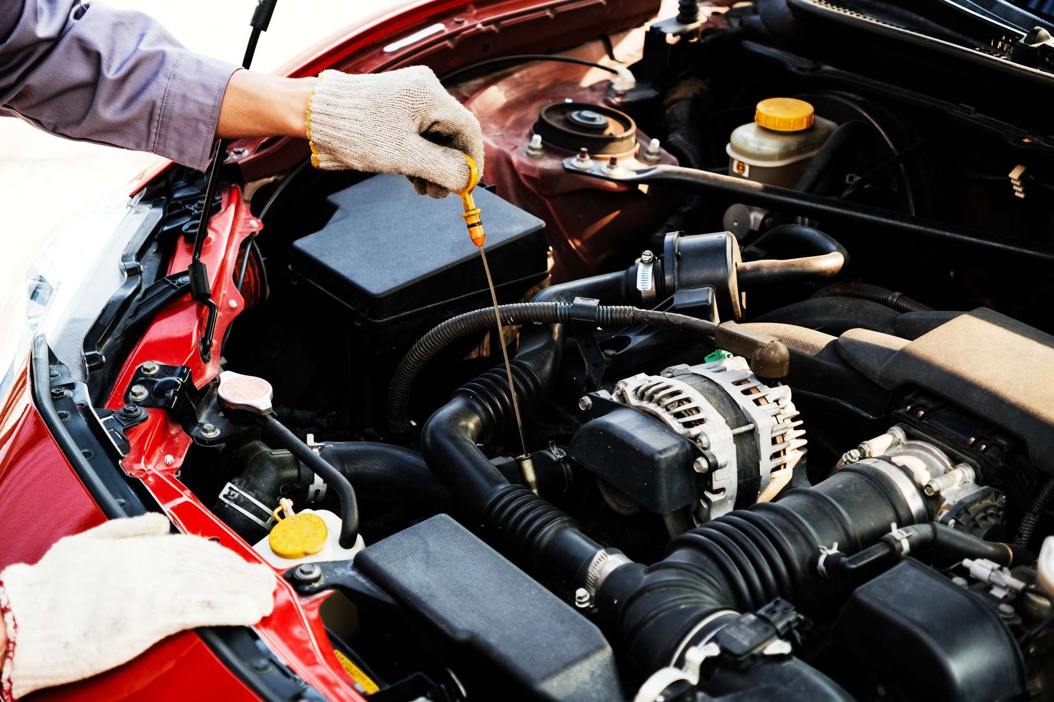 Gloved hand checking engine oil in a car with the hood open.