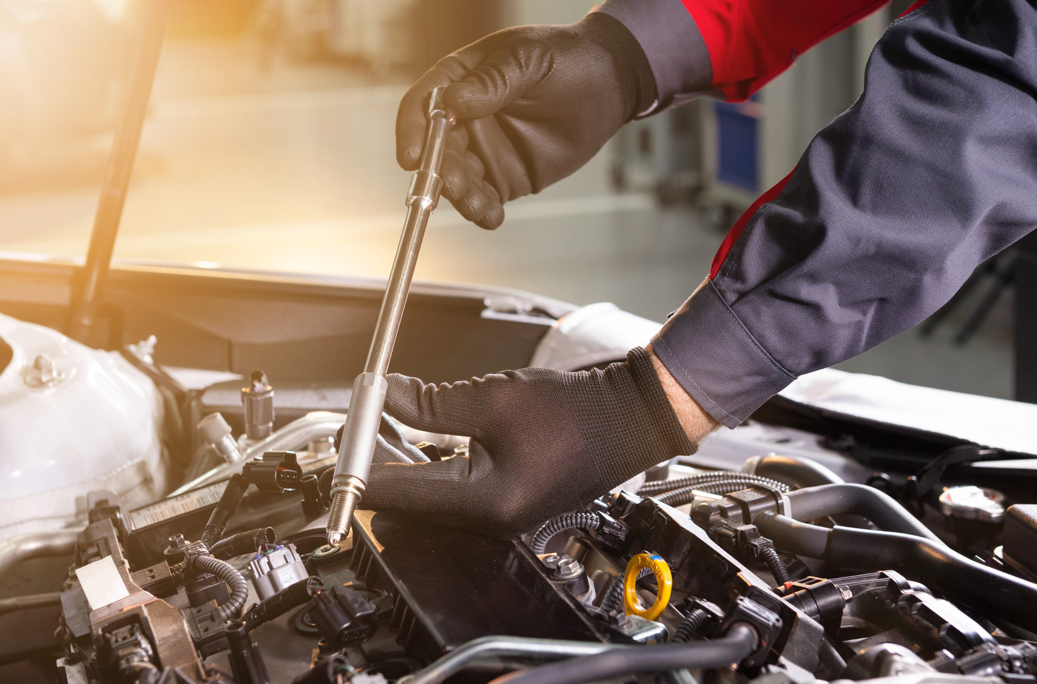 Mechanic using a wrench to fix a car engine while wearing black gloves.